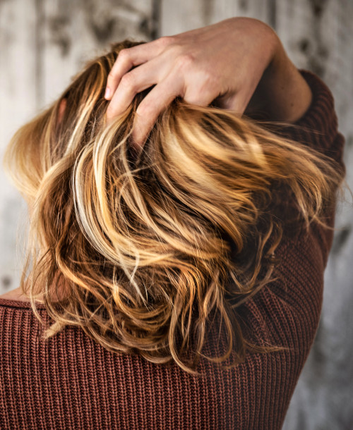 An image of the back of a lady putting her right hand through her beautiful luscious hair.